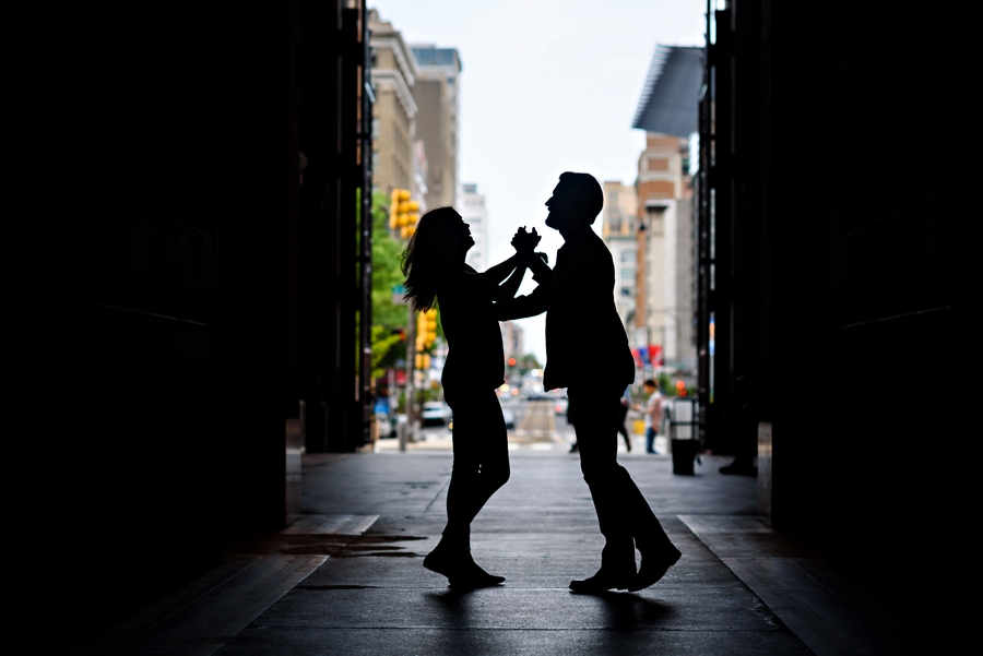A happy couple in love dance under city hall in philadelphia for their engagement session.